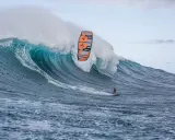 Ein Kitesurfer reitet eine riesige Welle bei Jaws, Hawaii. Die Welle bricht mit gewaltiger Kraft, während der Surfer mit seinem Kite in der Luft schwebt.