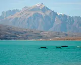 Boote treiben auf dem türkisfarbenen Lago di Santa Croce vor einer majestätischen Bergkulisse.