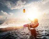 Kitesurferin genießt das Rhodos Surfen im goldenen Abendlicht, spritzt Wasser auf.