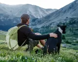 Mann mit Hund und Rucksack in den Bergen. Nach einer Wanderung ist der Rucksack reinigen eine gute Idee, bevor es weitergeht.