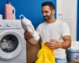 Mann hält Waschmittel und gelbes Trikot bereit, um die Wäsche zu waschen.