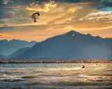 Kitesurfer gleiten über die Wellen am Chiemsee, während die Sonne hinter den Bergen untergeht. Ein traumhafter Abend für Windsurfen.