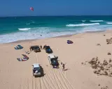 Kitesurfer bereiten sich auf das Windsurfen auf den Kapverden vor. Mehrere Kites liegen am Strand neben Autos.