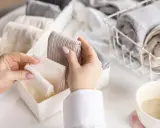 Hände sortieren gefaltete Kleidung, darunter auch warme **Wandersocken**, in Behälter.