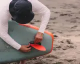 Mann mit Hut befestigt die rote Finne an einem aufblasbaren SUP-Board. Gute SUP-Pflege beginnt mit dem richtigen Zubehör.