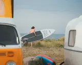 Mann mit SUP-Board am Strand von Fehmarn, bereit für die Wellen. Wohnmobile im Vordergrund.