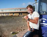 Bekannte deutsche Windsurfer: Ein Mann mit Sonnenbrille und Shaka-Geste lehnt an einem blauen Bus vor dem Centro Internacional de Windsurfing.