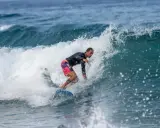 Ein Surfer reitet eine Welle vor Zypern. Er trägt ein schwarzes Rashguard und bunte Boardshorts.