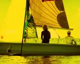 Zwei Segler auf einem Boot vor Hiddensee, bereit für Surf und Segel. Möwen beobachten das Geschehen.