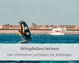 Person lernt wingfoilen auf dem Meer, mit einem Boot und Gebäuden im Hintergrund. Der ultimative Leitfaden für Anfänger.