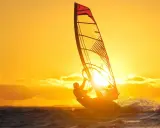 Ein Windsurfer genießt die untergehende Sonne am Ammersee. Das goldene Licht taucht die Szene in warme Farben.