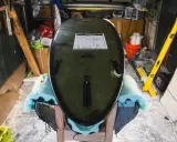 Surfboard liegt auf Ständer, bereit für die **Surfboard Reparatur**. Werkzeuge und Materialien im Hintergrund.