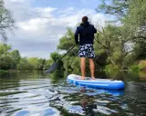 Mann auf SUP-Board auf ruhigem Fluss, umgeben von grünen Bäumen. Perfekt, um zu sehen, wo man stand up paddeln kann.