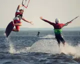 Zwei Kitesurfer springen und reichen sich die Hände auf dem Steinhuder Meer. Ein weiterer Surfer im Hintergrund.