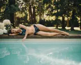 Frau liegt am Poolrand, ihr Badeanzug mit Blattmuster ist frisch gewaschen und bereit für die Sonne.