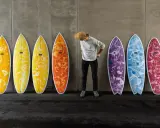 Mann mit Hut steht vor bunten Surfbrettern, bereit für das Wellenreiten.