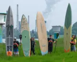 Fünf Personen mit SUP-Boards und Paddeln vor einer Industrieanlage. Die Boards zeigen fortgeschrittene SUP-Technik.