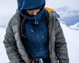 Person in Daunenjacke im Schnee. Die Jacke ist grau und blau, mit gelben Akzenten. Perfekt für das Daunenjacke waschen nach einer Bergtour.