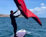 Mann mit rotem Wingboard auf dem Wasser vor Costa Calma. Perfekter Tag für Wassersport am Ion Club.