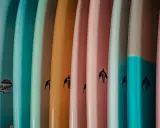 Reihe bunter Surfboards in Pastelltönen. Welches Surfboard passt zu mir? Die Auswahl ist groß, von hellblau bis rosa.