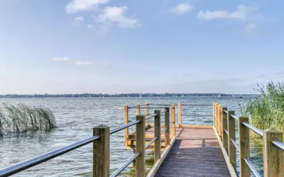 Holzsteg am Zwischenahner Meer mit Segelbooten am Horizont und Schilf am Ufer.