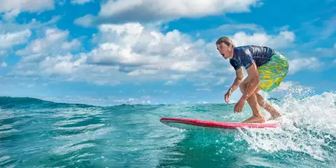 Ein Surfer reitet eine Welle vor der Küste der Dominikanischen Republik. Der Mann trägt ein blaues Shirt und bunte Badeshorts.
