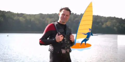 Mann in Neoprenanzug und Schwimmweste erklärt, wie funktioniert ein Neoprenanzug. Im Hintergrund eine stilisierte Windsurferin.