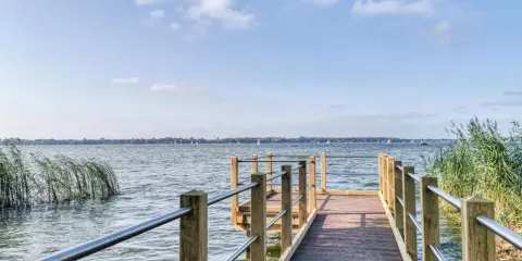 Holzsteg am Zwischenahner Meer mit Segelbooten am Horizont und Schilf am Ufer.
