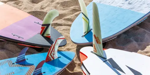 Mehrere Windsurfboards mit bunten Finnen liegen im Sand. Perfekt, wenn Sie ein Windsurfboard kaufen möchten.
