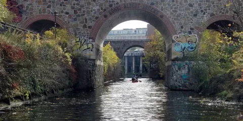 Kanus auf dem Fluss unter einer Steinbrücke mit Graffiti. Sup Leipzig!
