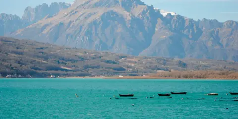 Boote treiben auf dem türkisfarbenen Lago di Santa Croce vor einer majestätischen Bergkulisse.
