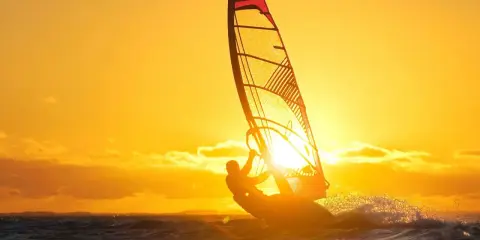 Ein Windsurfer genießt die untergehende Sonne am Ammersee. Das goldene Licht taucht die Szene in warme Farben.