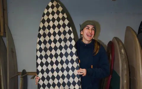 Frau lacht und hält ein selbstgebautes Surfbrett mit Rautenmuster.