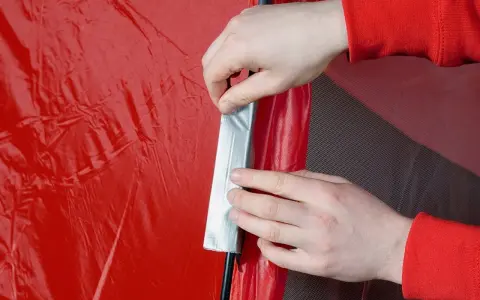 Hände flicken ein rotes Zelt mit silbernem Klebeband.