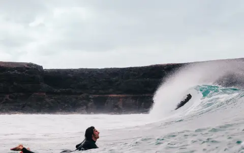 Surfer wartet auf die perfekte Welle vor der Felsküste. Windsurfen Fuerteventura.