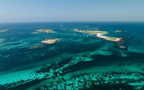 Türkisblaues Wasser umgibt die Glenan Inseln mit einem Leuchtturm auf einer kleinen Insel.