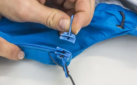 Hände tauschen den blauen Reißverschluss-Zipper an einer Jacke aus.