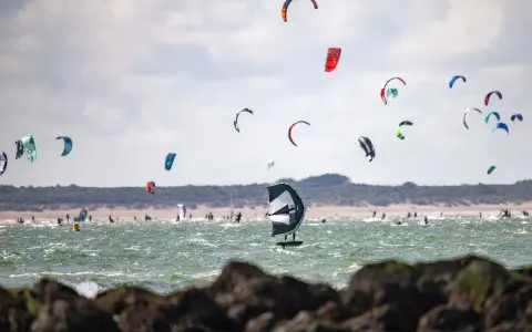 Viele bunte Kites und Surfer bevölkern das Meer am Brouwersdam Zeeland. Ein Kitefoiler schwebt über dem Wasser.