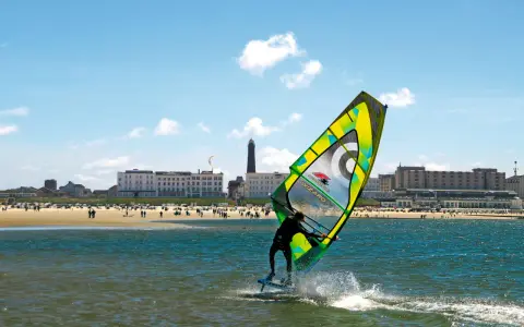 Windsurfer auf dem Meer vor Borkum, im Hintergrund der Strand mit Menschen und Hotels.