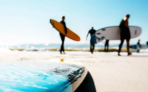 Surfer in Holland tragen ihre Boards zum Wasser. Die Sonne scheint, die Wellen brechen.