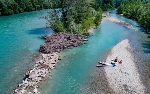 Standup paddling am Feldmarksee: Zwei Personen ruhen sich auf einer Kiesbank aus, während zwei Boards im türkisfarbenen Wasser liegen.