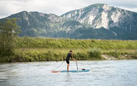 Mann auf SUP-Board, der geradeaus fährt, mit Bergen im Hintergrund.