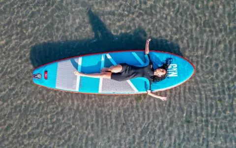 Frauen entspannt auf einem SUP-Board in NRW liegend. Das Board ist blau mit roten Akzenten.