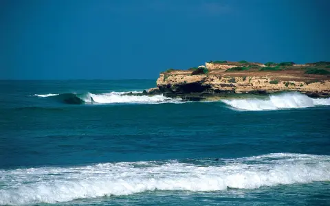 Türkisblaue Wellen brechen sich an einer felsigen Küste. Ein perfekter Tag für capo mannu surf.