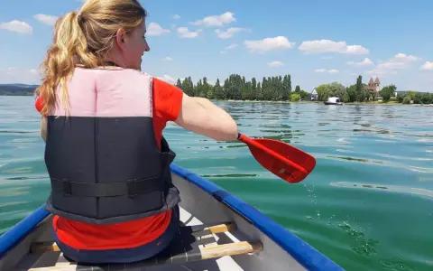 Frau paddelt im Kanu auf einem See, genießt sup touren deutschland. Im Hintergrund: Ufer mit Bäumen und Häusern.