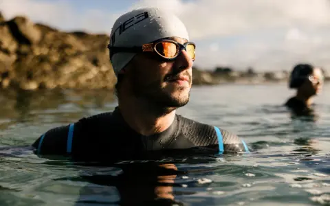Mann mit Schwimmbrille und Badekappe im Wasser, bereit für das Schwimmen. Die Schwimmbrille reinigen ist wichtig für klare Sicht.