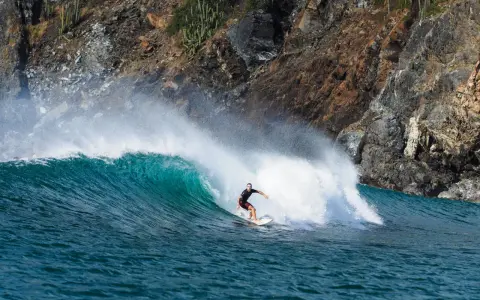 Surfer reitet eine grüne Welle vor einer felsigen Küste. Perfekt für die Surf-App, um die nächste Session zu planen.