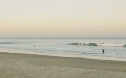 Ein Surfer geht ins Meer, um Cornwall zu surfen. Sanfte Wellen brechen am Strand.