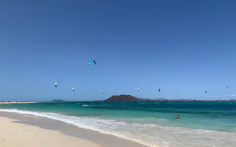 Kitesurfer tanzen über das türkisfarbene Wasser am Flag Beach Corralejo. Ein einsamer Schwimmer genießt die Sonne.