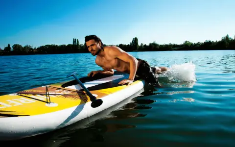 Mann liegt auf SUP-Board, paddelt mit Armen im Wasser. Perfekt für eine SUP Tour auf dem See.